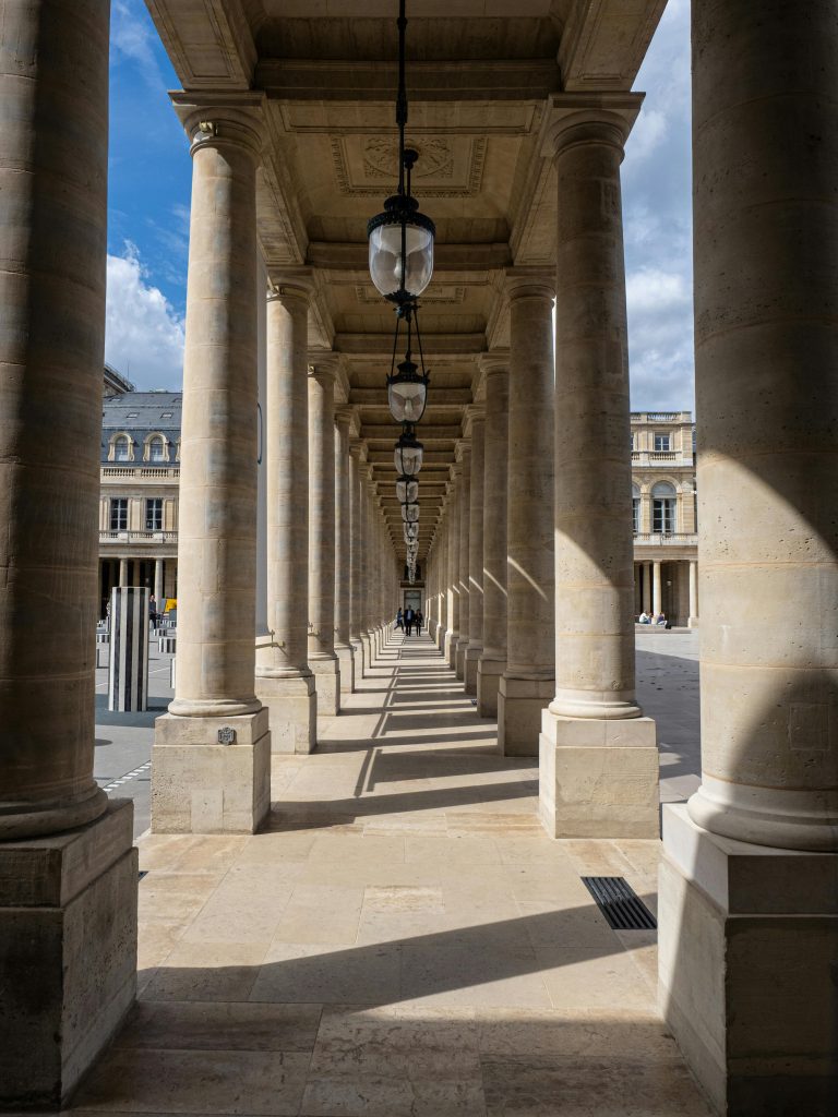 Elegant stone columns of Palais Royal, Paris, casting dramatic shadows under a blue sky.